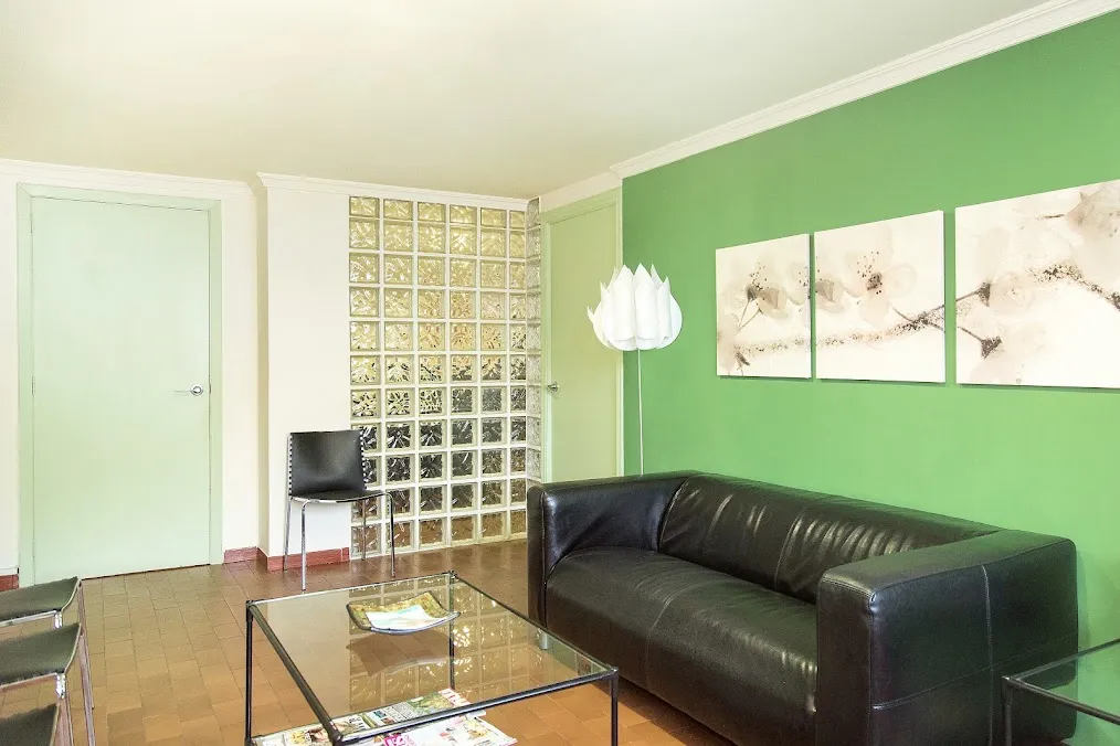 Sala de espera de Odontos, Clínica Dental, con sofá de piel, pared verde y luz natural
