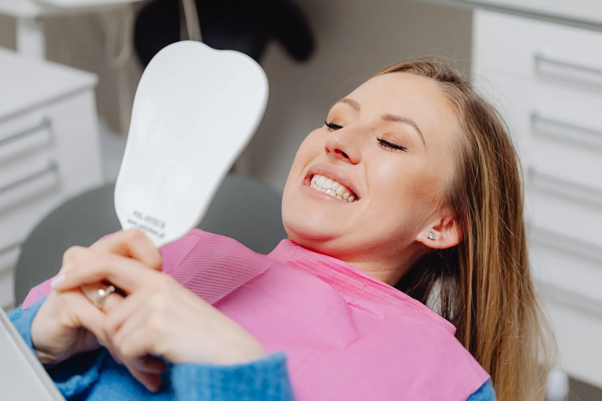 Paciente sonriendo satisfecha mientras se mira los dientes en un espejo de mano